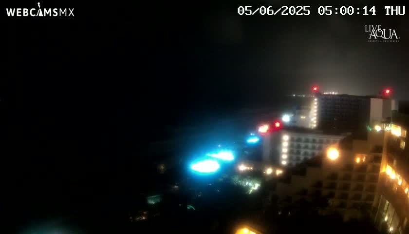 A nighttime view of illuminated buildings near a body of water, under hazy conditions.