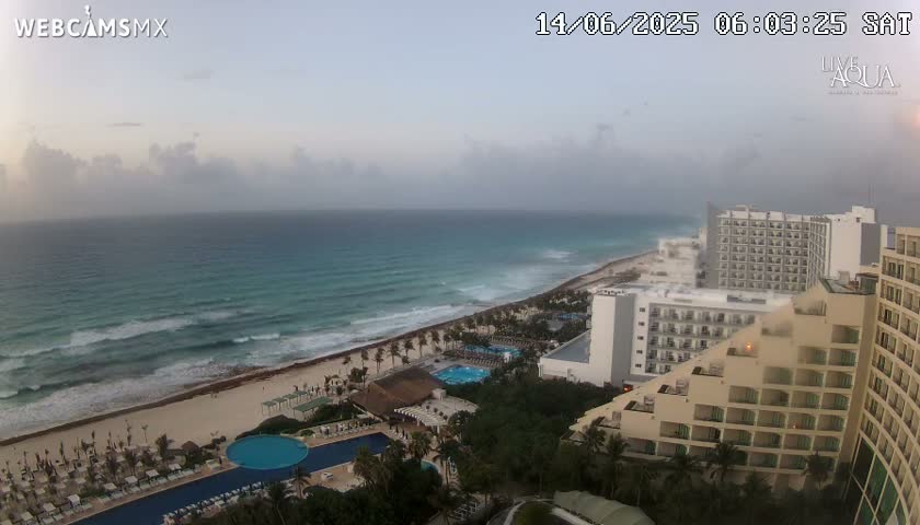 An overcast sky hangs over a beach with turquoise water and moderate waves, where several large hotels are situated along the shoreline.
