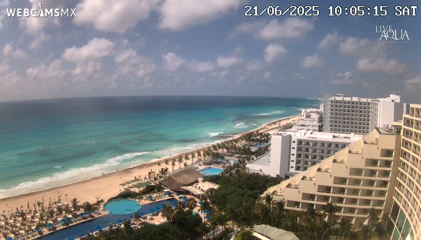 A partly cloudy day shows a beach with turquoise water and multiple hotels along the coast.