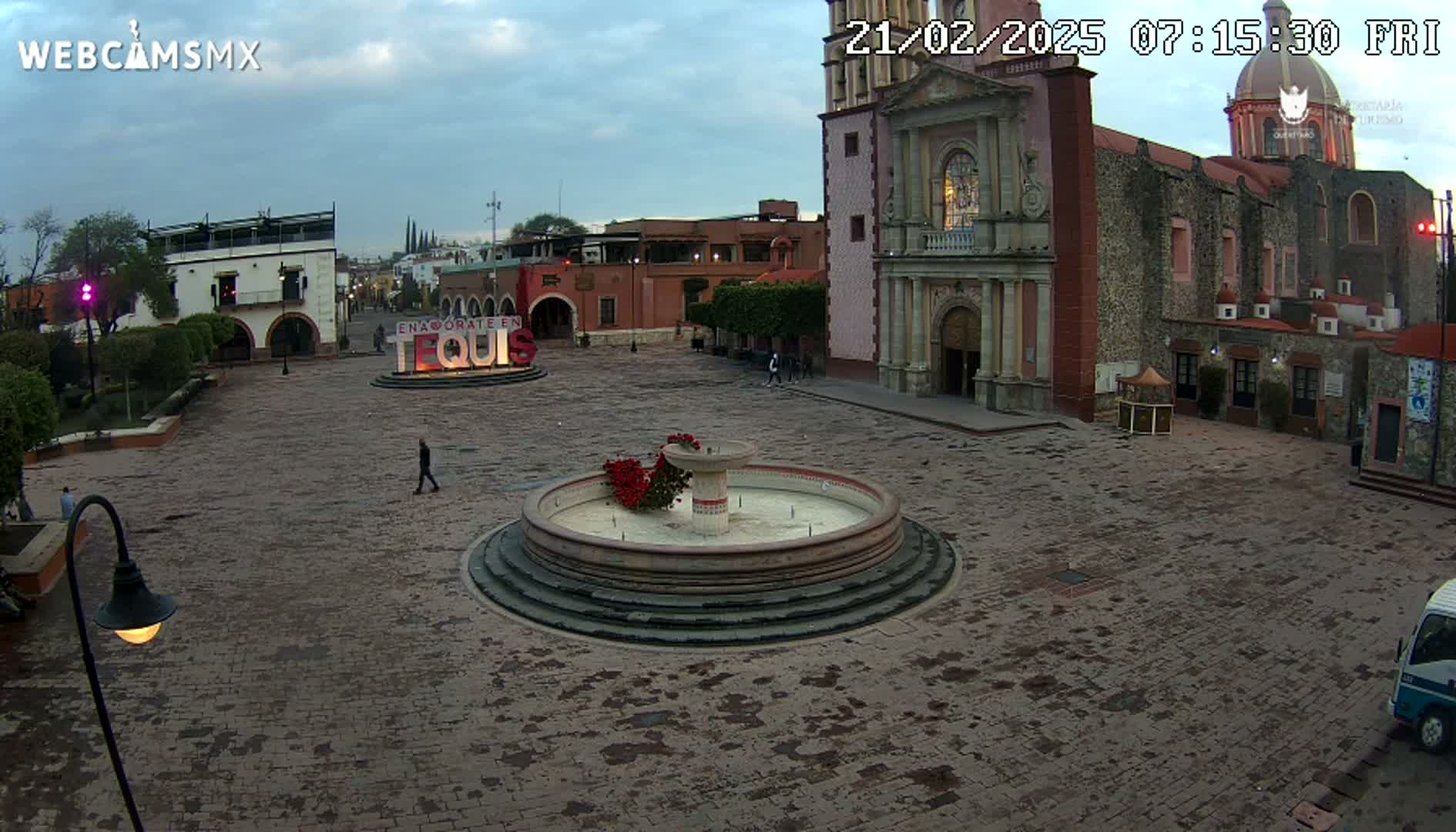 A town square with a fountain, a large church, and several buildings under an overcast sky.