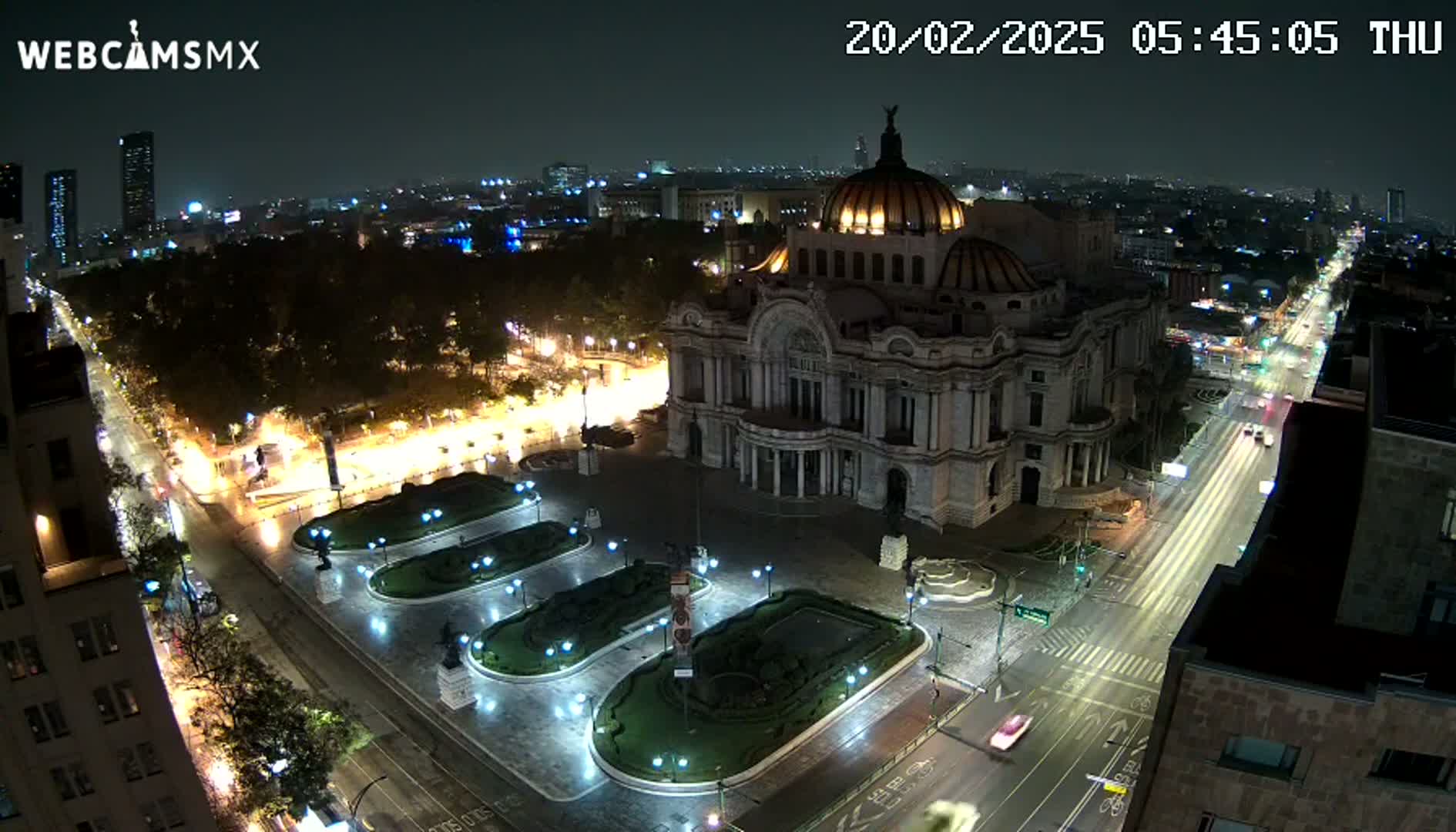 A nighttime aerial view of a large, ornate building in a city, with wet streets and some traffic visible.