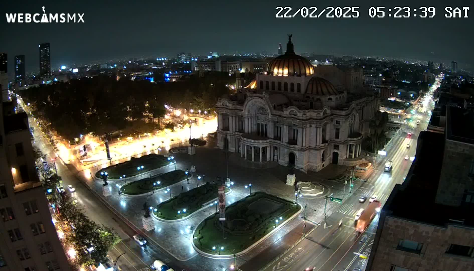 A nighttime, aerial view of Palacio de Bellas Artes in Mexico City, showing wet streets and surrounding city lights.