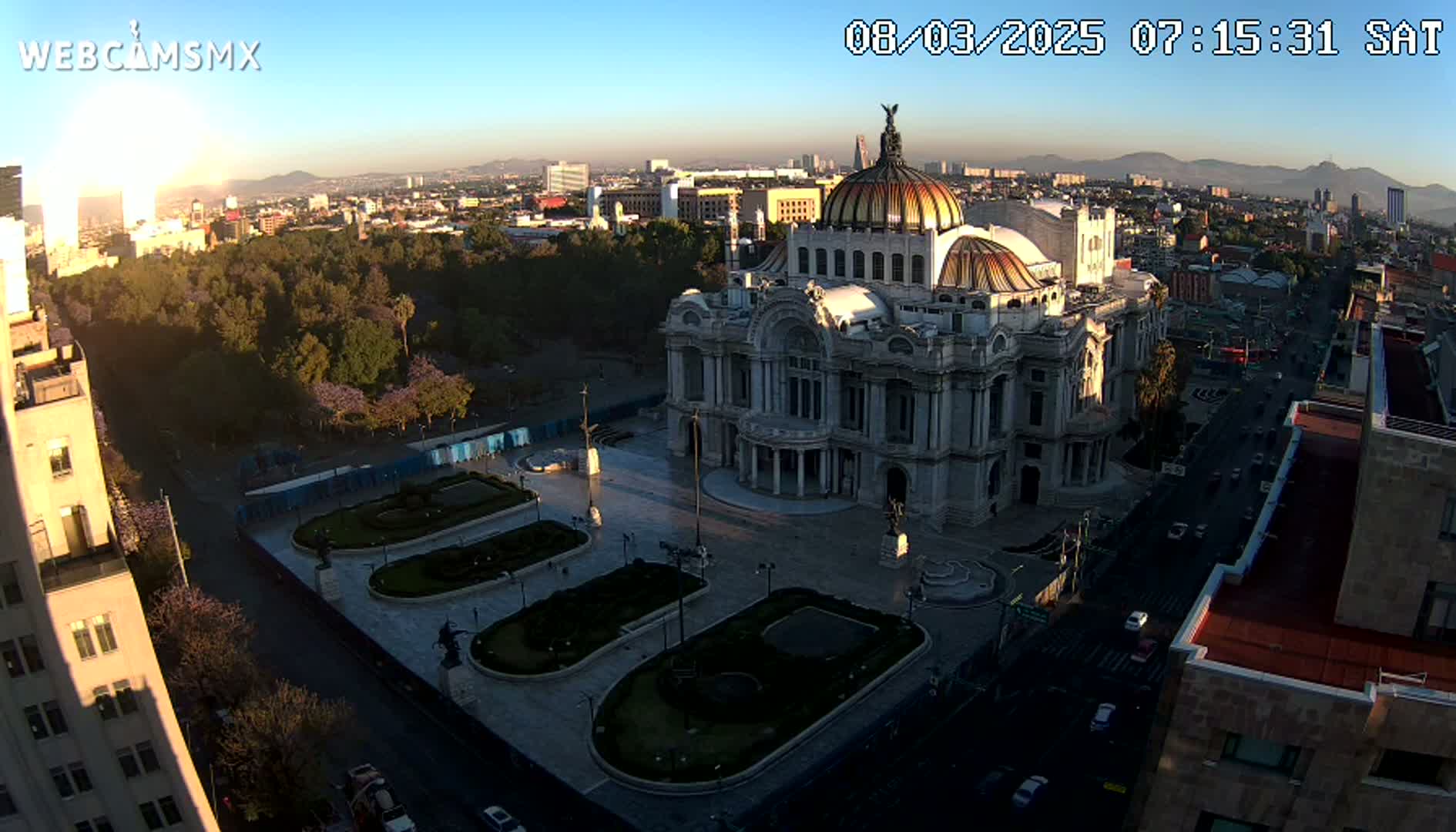 An aerial view shows Palacio de Bellas Artes in Mexico City on a clear, sunrise-lit morning, with surrounding streets and a park.