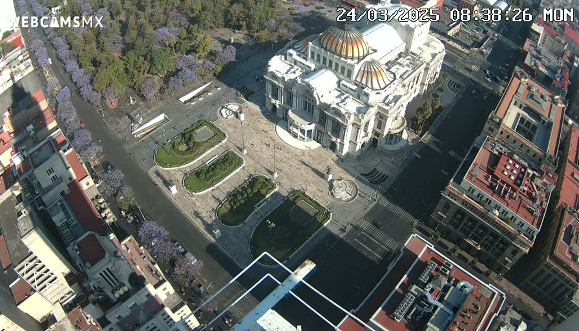 An aerial view of a large plaza with a grand building in the center, surrounded by city streets and buildings under a sunny sky.