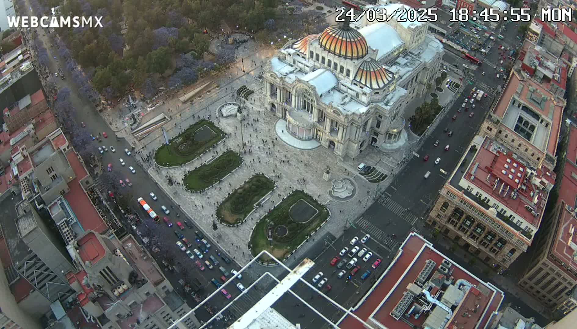 An aerial view shows a large building with a dome in a city square surrounded by streets and other buildings during the evening.
