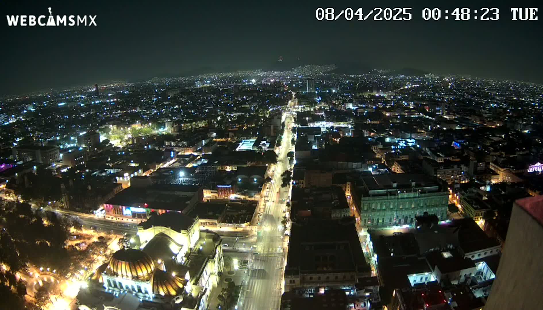A nighttime aerial view of a city with a long, brightly lit street running through its center, under a clear sky.