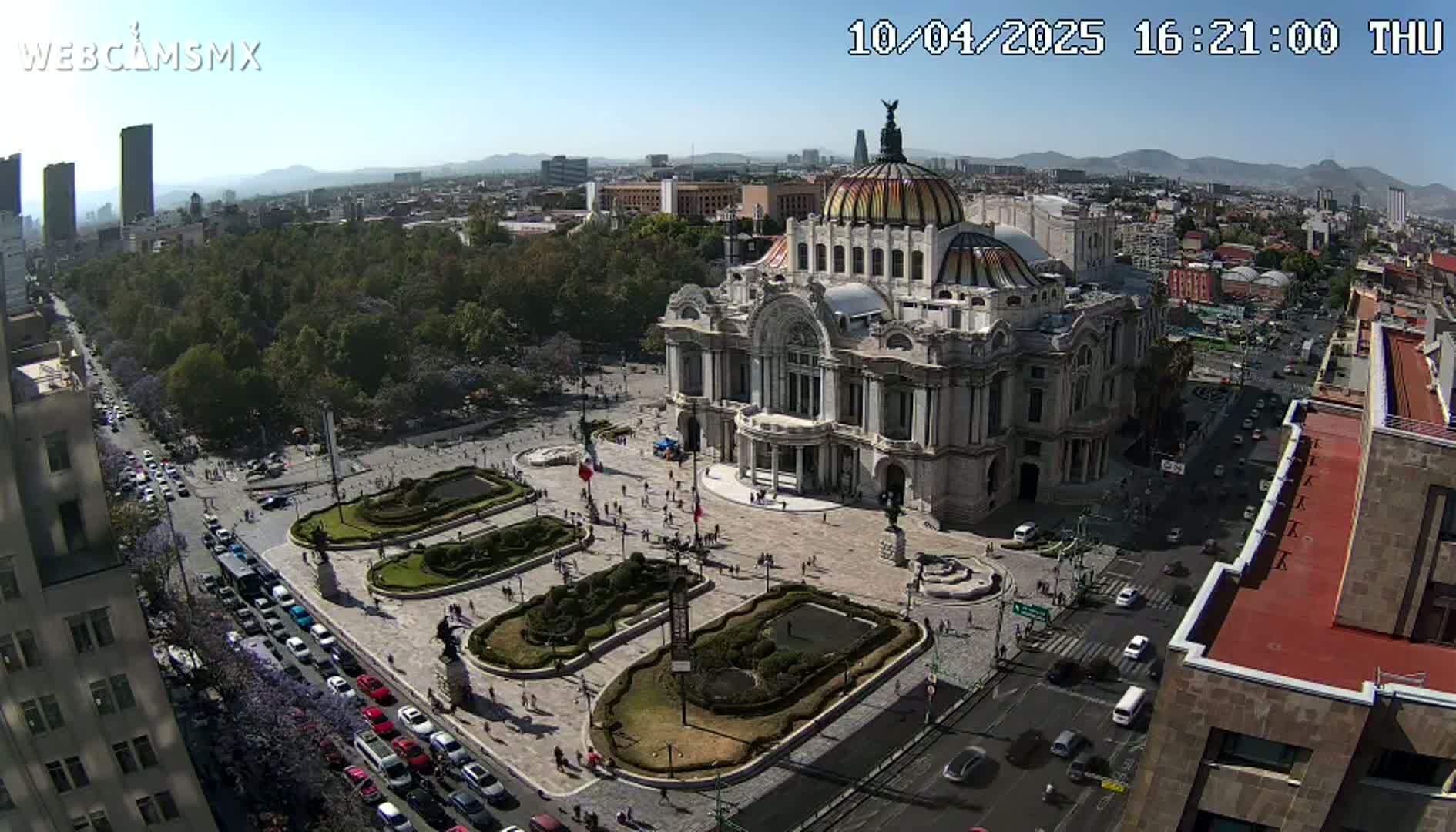 An aerial view shows Palacio de Bellas Artes in Mexico City on a sunny day, surrounded by a plaza with landscaping and busy streets.