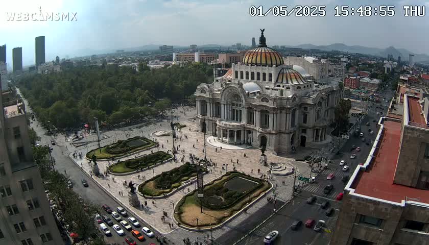 An aerial view of a large, ornate building surrounded by a plaza with landscaping and streets filled with cars, under a mostly clear sky.