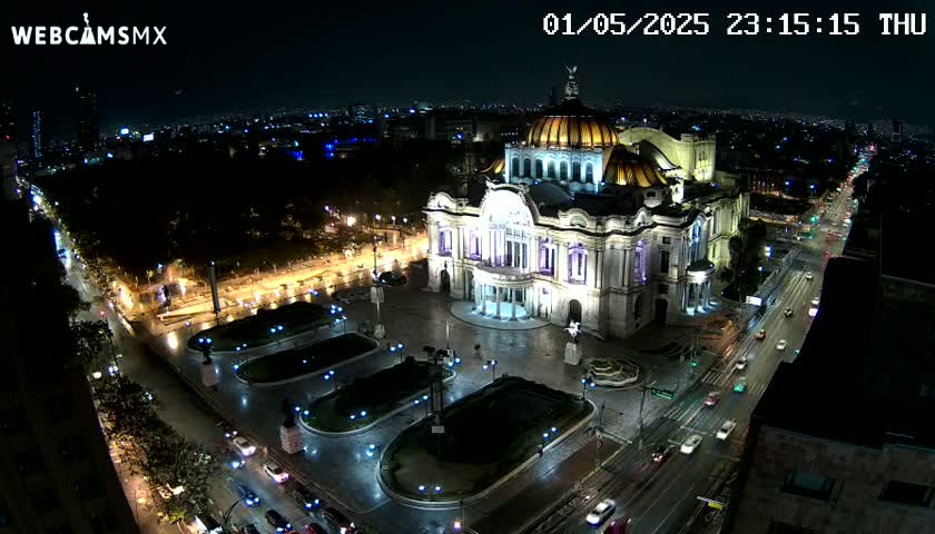 A brightly lit palace-like building sits in a plaza at night, with city lights and traffic visible in the surrounding area under a clear, dark sky.