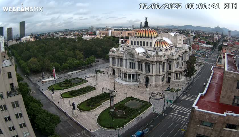 An aerial view of Palacio de Bellas Artes in Mexico City on an overcast day, showing the building surrounded by a plaza, roadways, and green spaces.