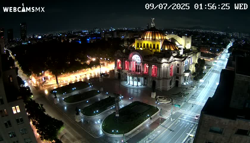 A brightly lit palace-like building stands in a plaza at night, with a city street extending from it, sparsely populated with cars under clear skies.