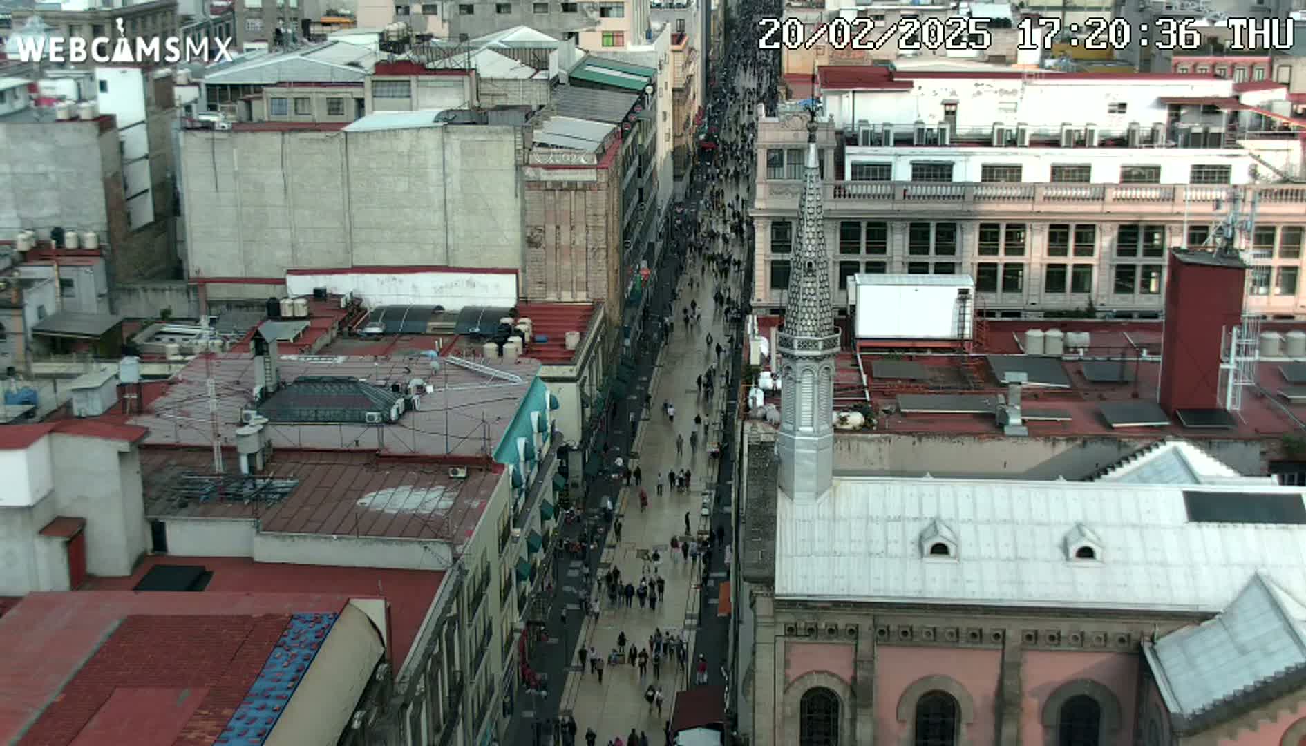 A high-angle view shows a crowded street in a city with many buildings, under a daytime sky.