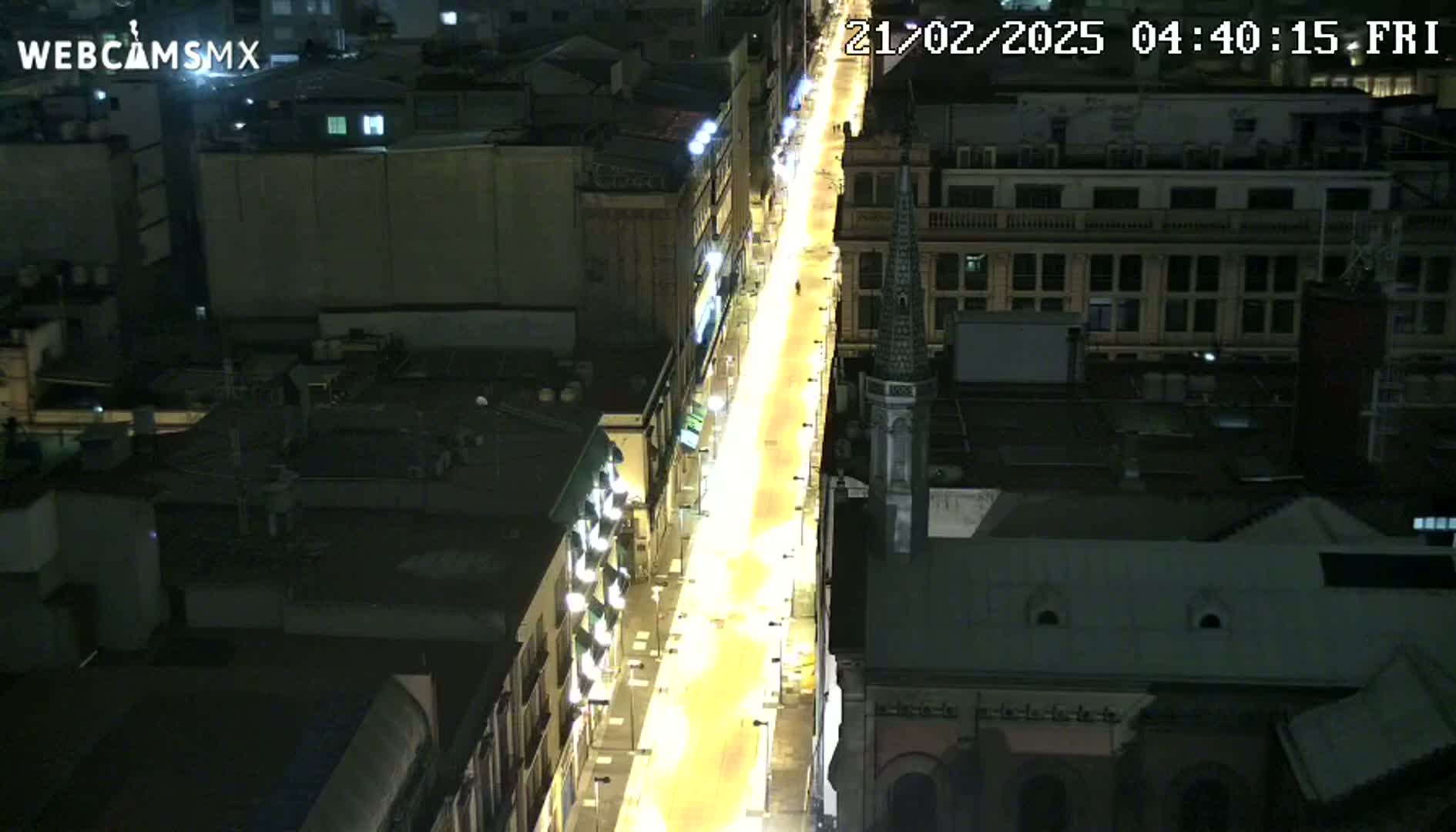 An aerial nighttime view of a brightly lit city street, flanked by buildings.