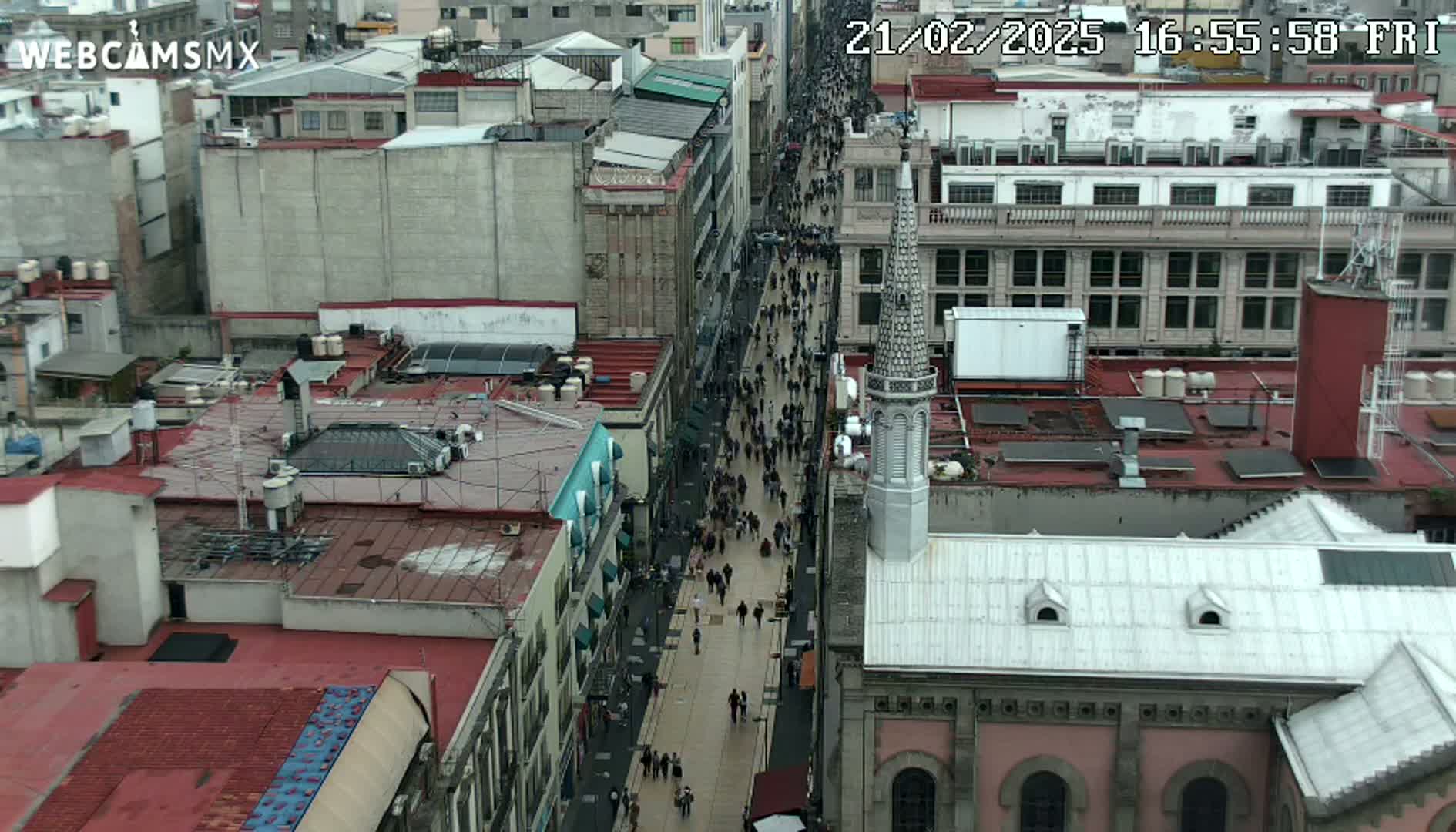 A crowded city street is viewed from above, with overcast weather conditions.