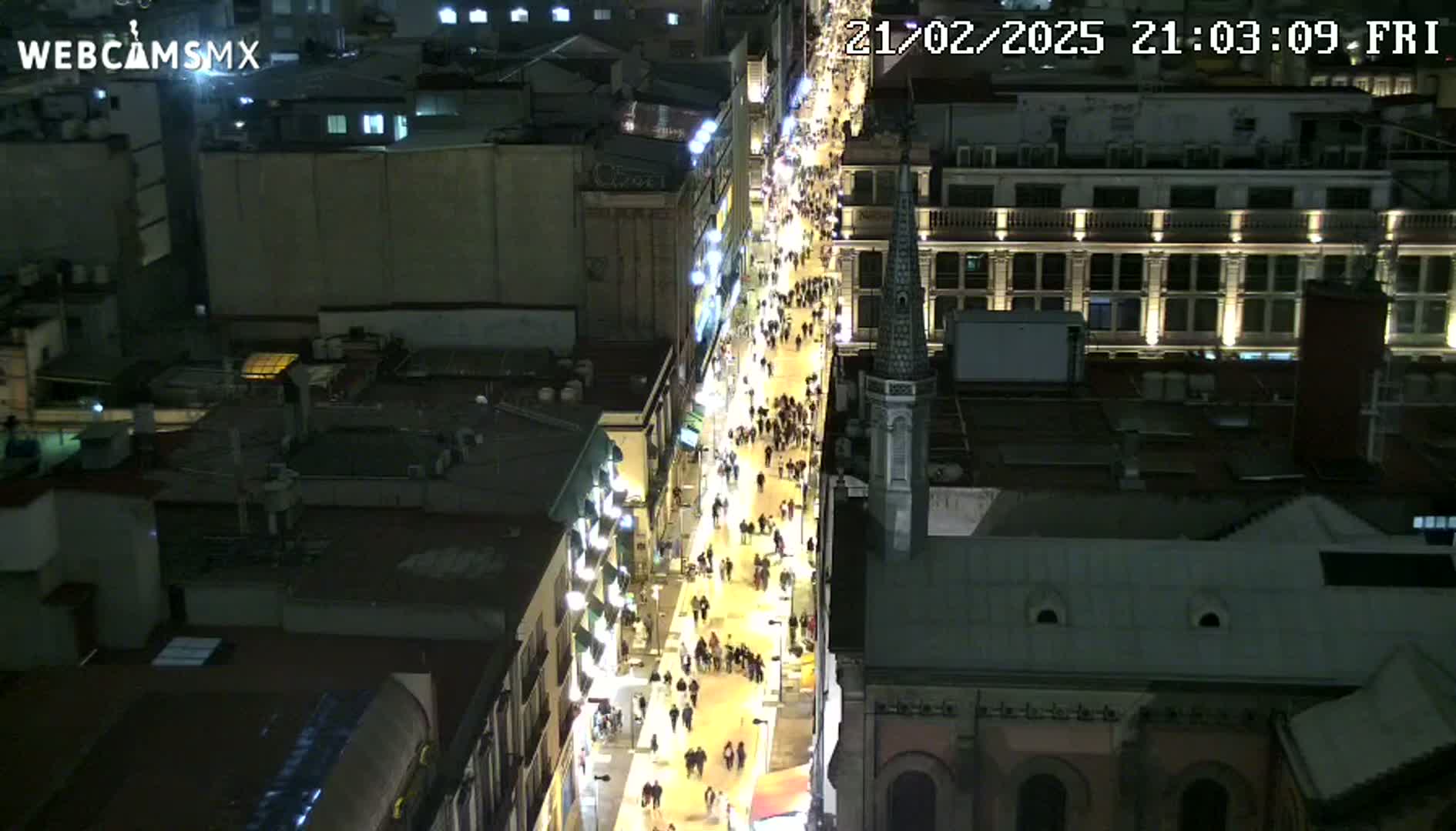 A nighttime, high-angle view shows a crowded pedestrian street lined with illuminated buildings.