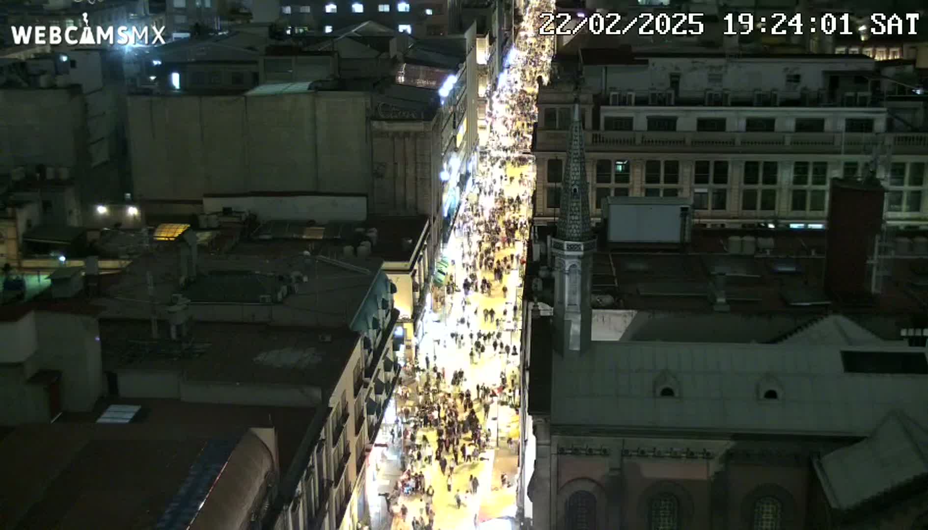 A nighttime, aerial view shows a crowded city street flanked by buildings.
