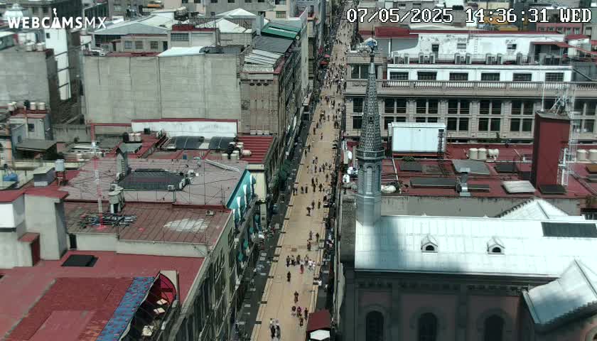 A high-angle, long shot of a city street with many pedestrians and buildings on a sunny day.