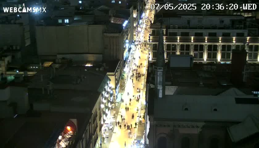 A nighttime, high-angle view shows a brightly lit city street bustling with pedestrians, flanked by buildings.