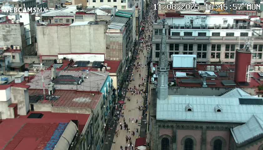 A high-angle view shows a crowded pedestrian street flanked by buildings, under an overcast sky.