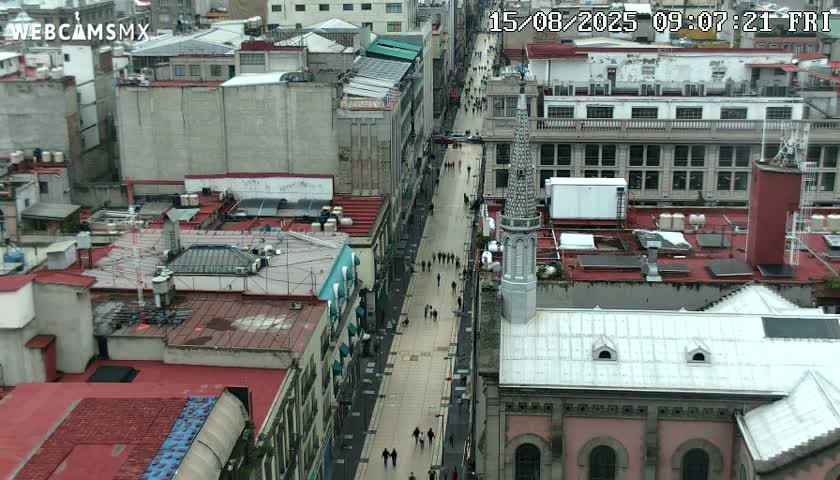 A high-angle view shows a crowded pedestrian street flanked by buildings, under an overcast sky.