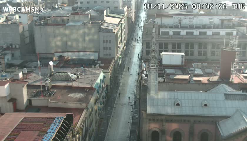 A high-angle view shows a crowded pedestrian street flanked by buildings, under an overcast sky.