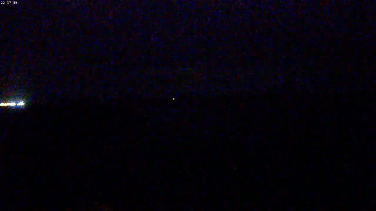 A nighttime scene shows a faint, horizontal line of light near the bottom and a small, distant light source higher up and slightly to the right.