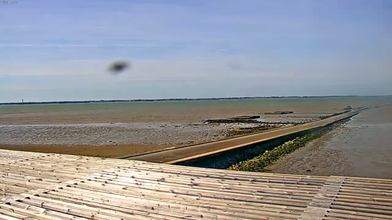 A long, low causeway extends into a calm, shallow body of water under a mostly clear sky.