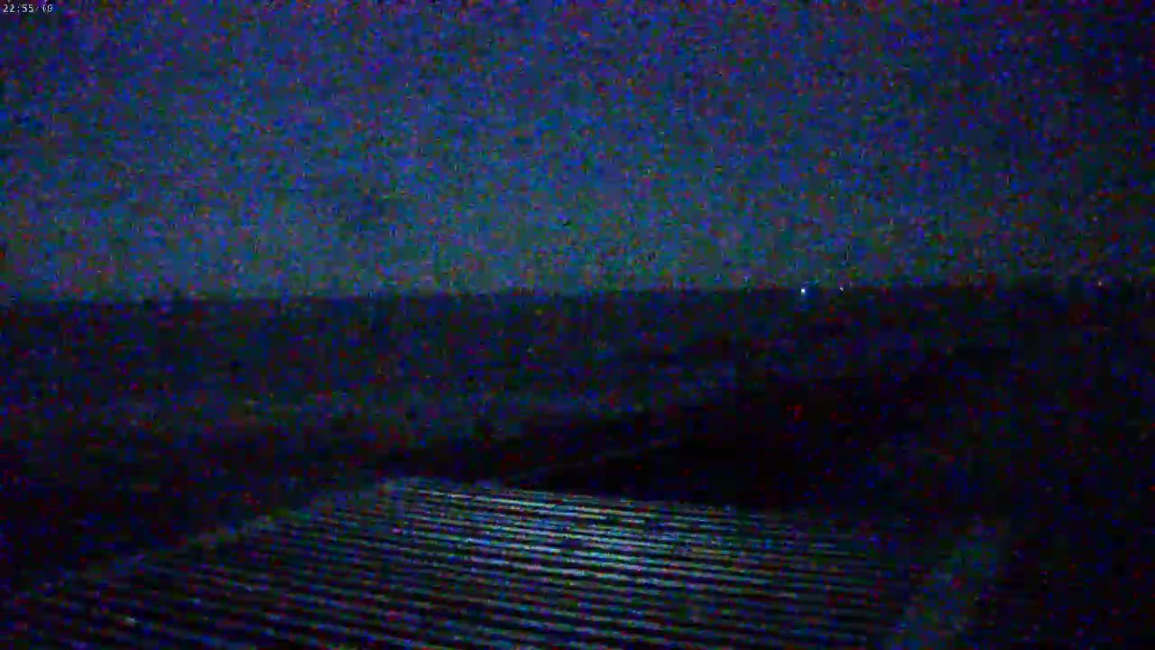 A nighttime view shows a dark, flat landscape under a mostly clear, dark blue sky, with a corrugated surface in the foreground.