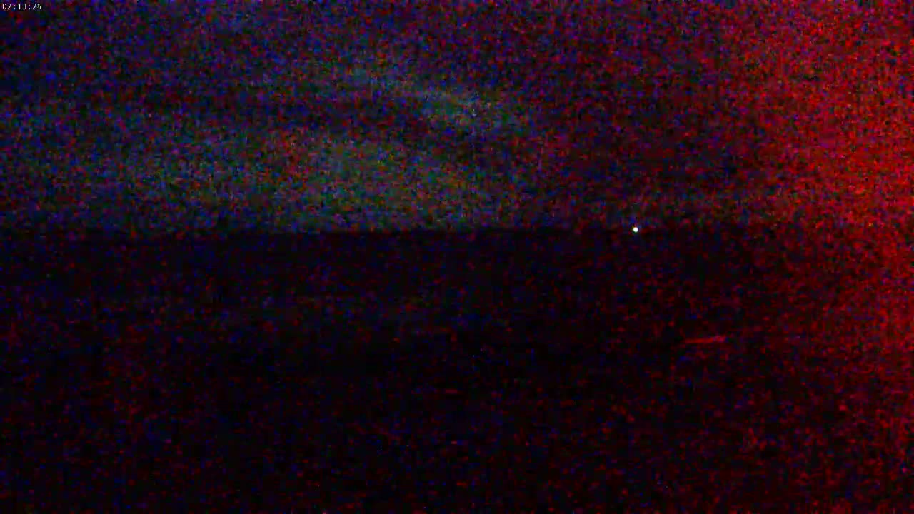 A dark, nighttime scene shows a mostly-clear sky with a few faint clouds above a dark landscape.