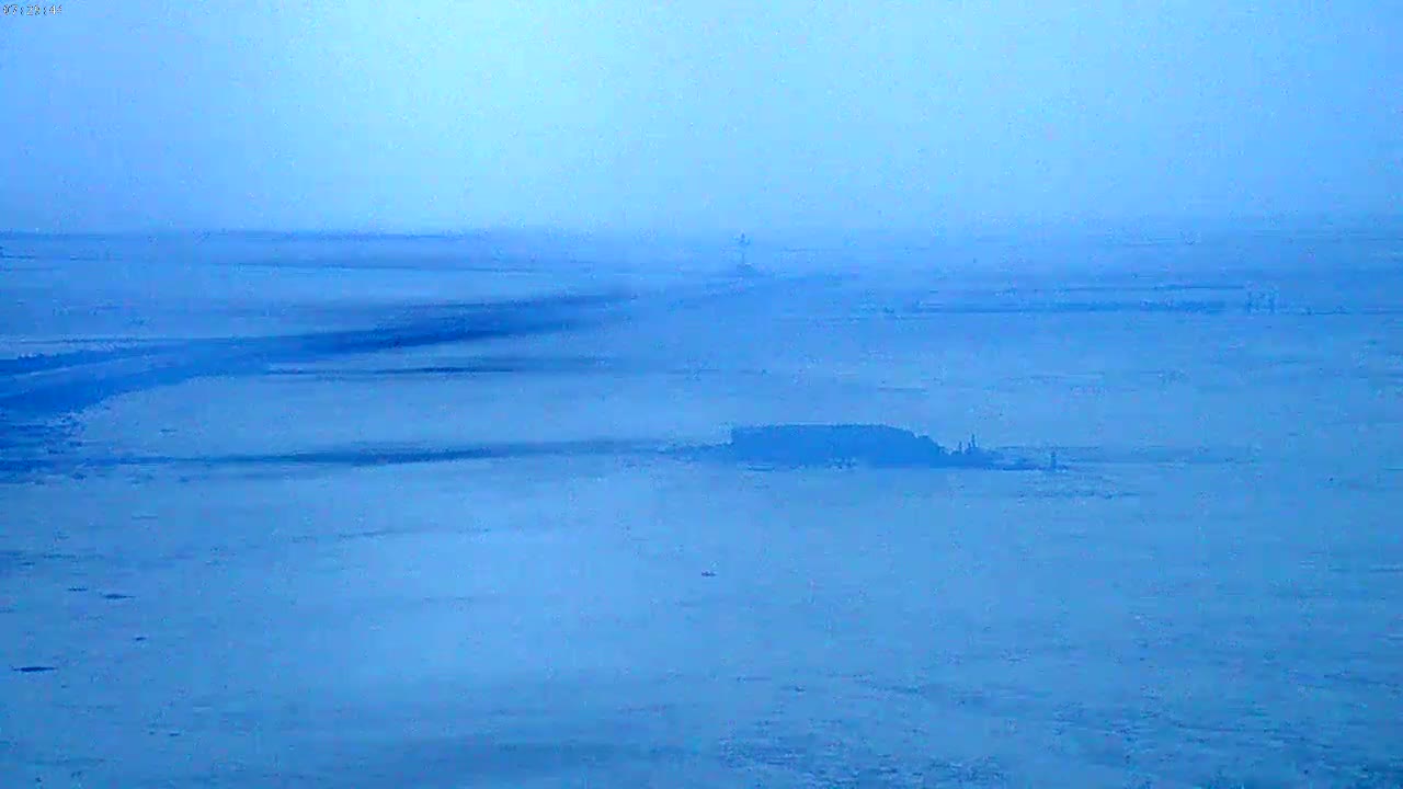 A hazy, light-blue expanse of water shows a dark, low-lying landmass in the middle distance.