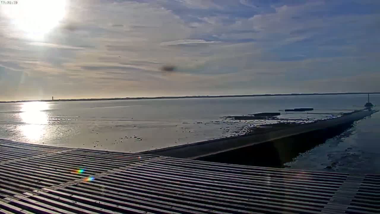 A long, low structure extends from a shoreline into a calm body of water under a partly sunny sky.