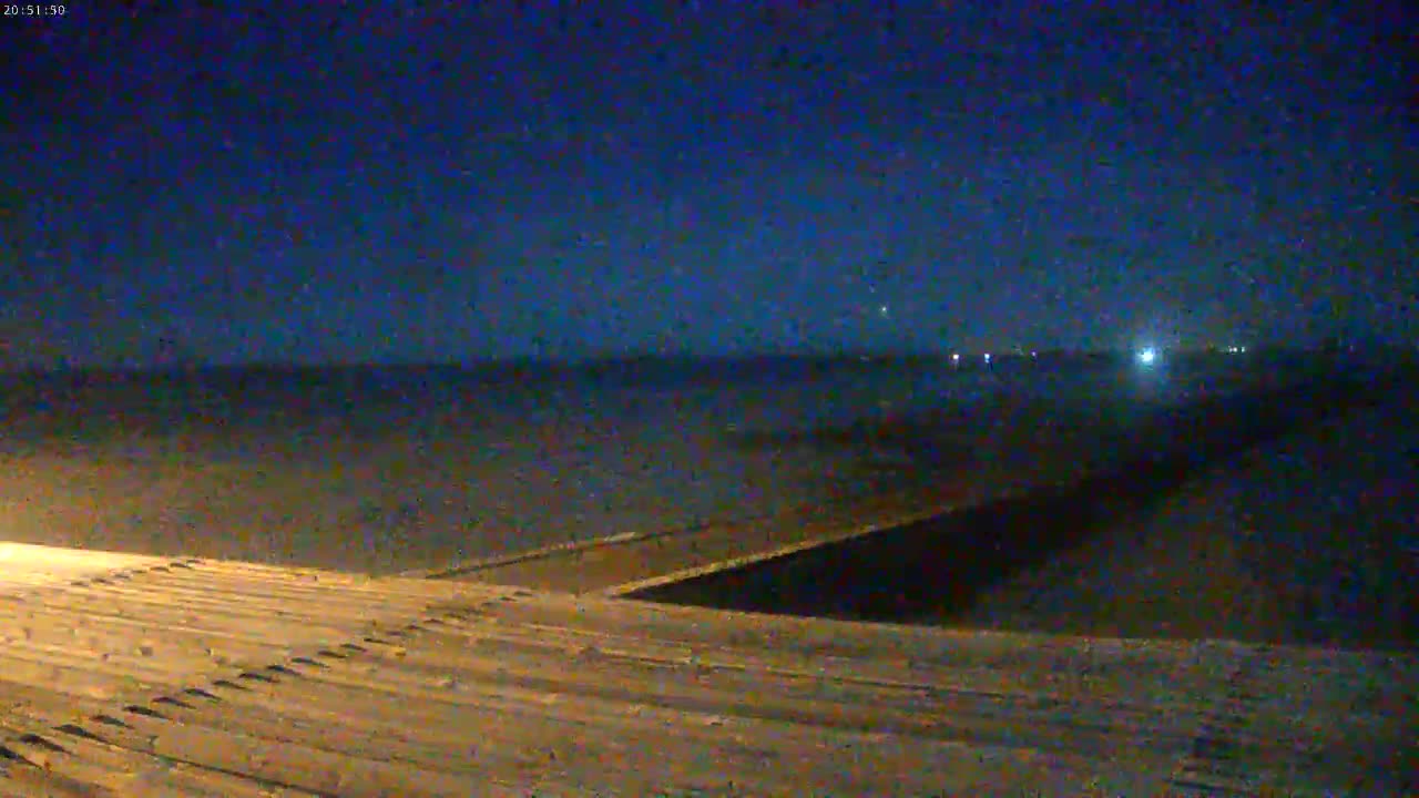 A nighttime view shows a sloped, textured surface extending from the bottom of the frame toward a dark body of water under a clear, dark blue sky.
