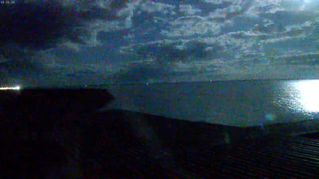 A dark, nighttime view of a calm body of water under a cloudy sky.