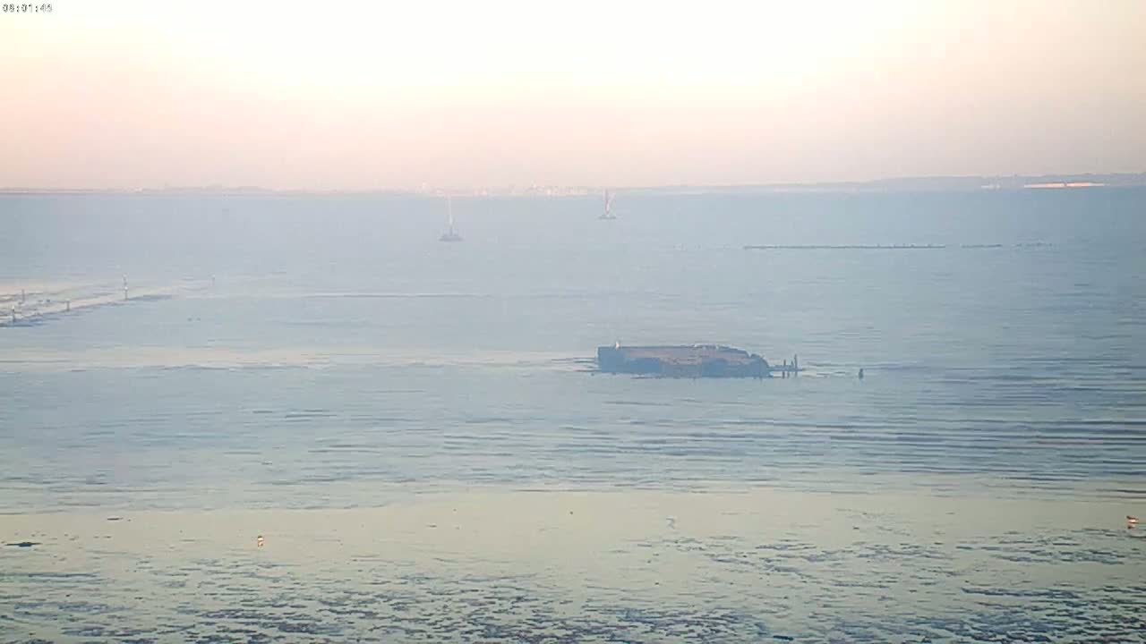 A hazy, calm body of water shows a partially submerged structure and distant land in the background.