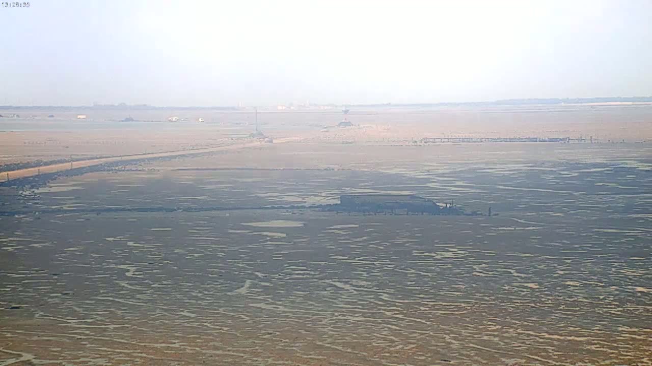 A hazy, expansive flatland with scattered pools of water and a distant road stretches to the horizon.