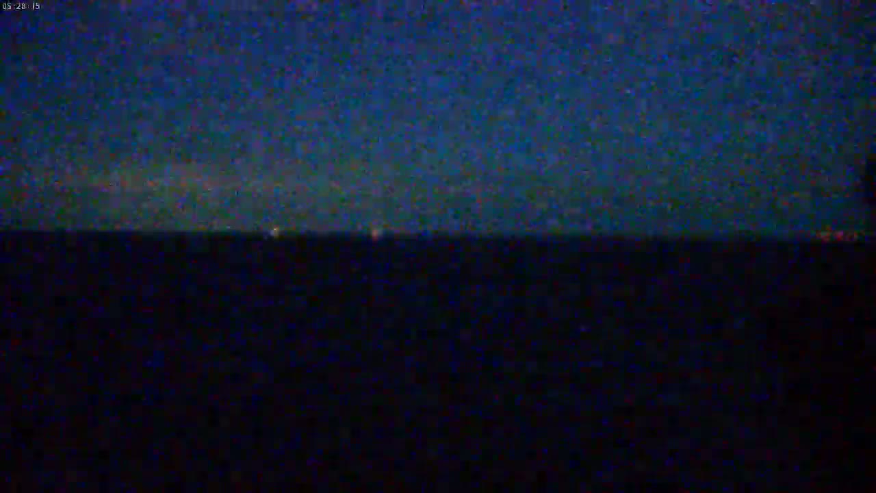 A dark, nighttime scene shows a horizon line separating a darker lower area from a slightly lighter, dark blue sky.