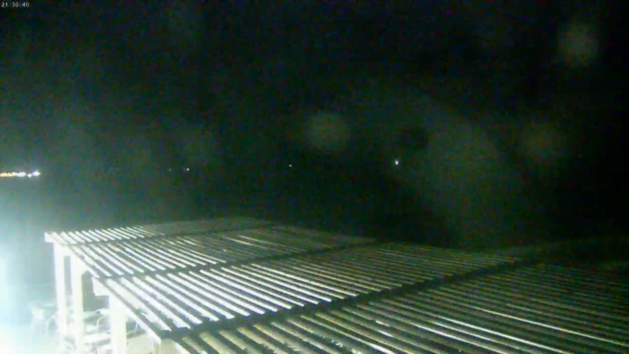 A slatted pergola is visible in the foreground under a dark, nighttime sky with faint, distant lights.