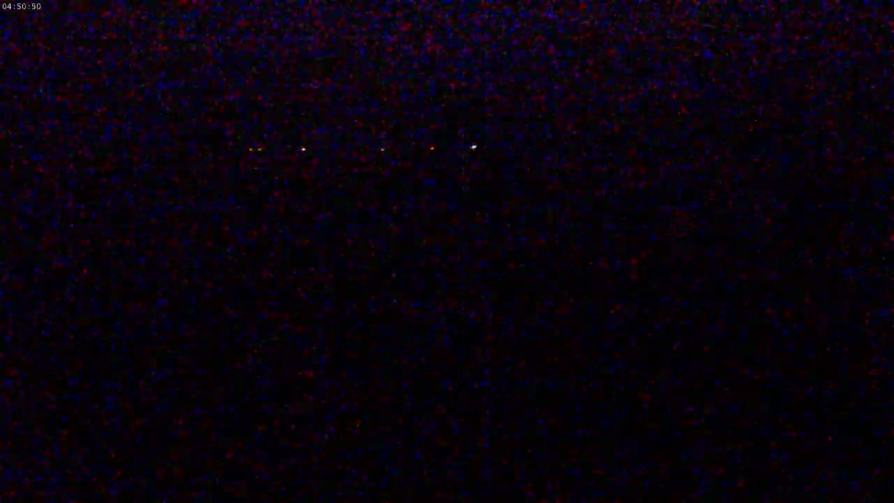 A nighttime image shows a dark landscape with a few small, distant lights.