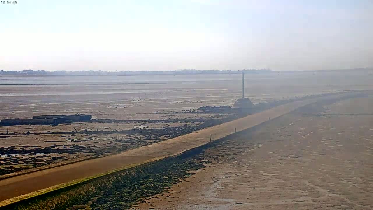 A long road stretches across a hazy, flat expanse of mudflats under a bright, clear sky.