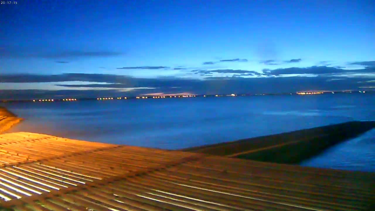 A dark-blue body of water stretches to a distant shoreline dotted with lights under a twilight sky.
