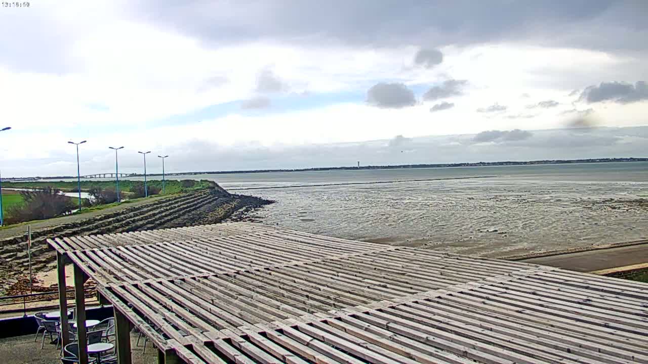 A wooden pergola overlooks a calm, wide body of water under a mostly cloudy sky.