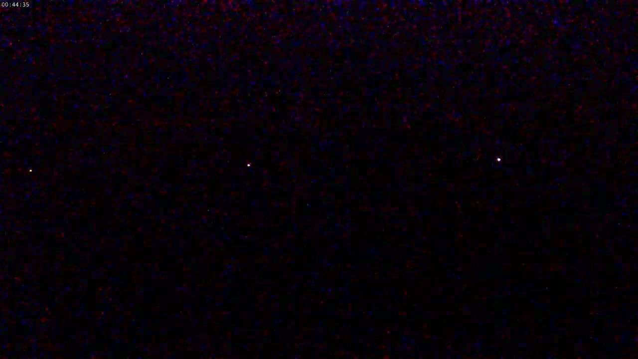 A nighttime sky shows three faint points of light against a dark, speckled background.