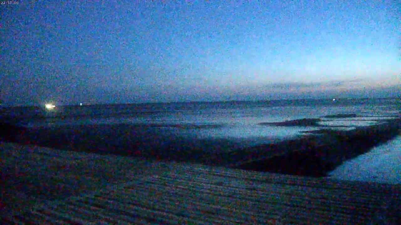A dark beach slopes down to a calm, dark blue ocean under a twilight sky.