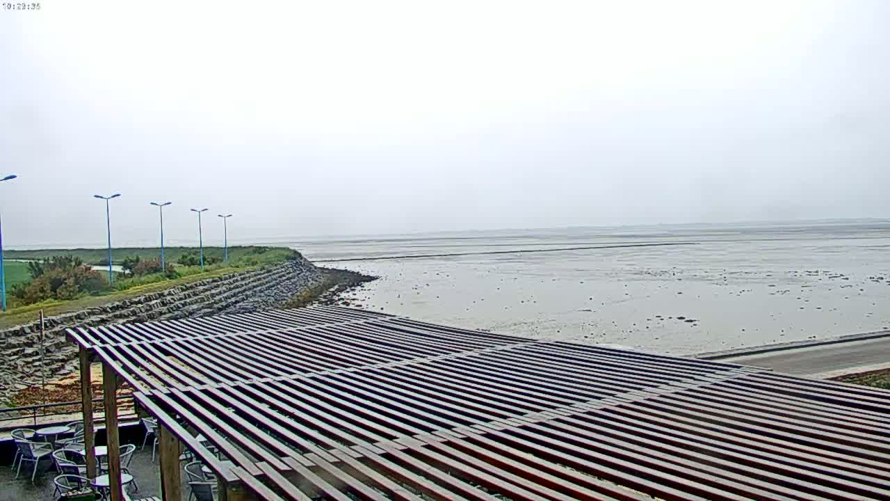 A slatted wooden pergola overlooks a calm, gray body of water on an overcast day.