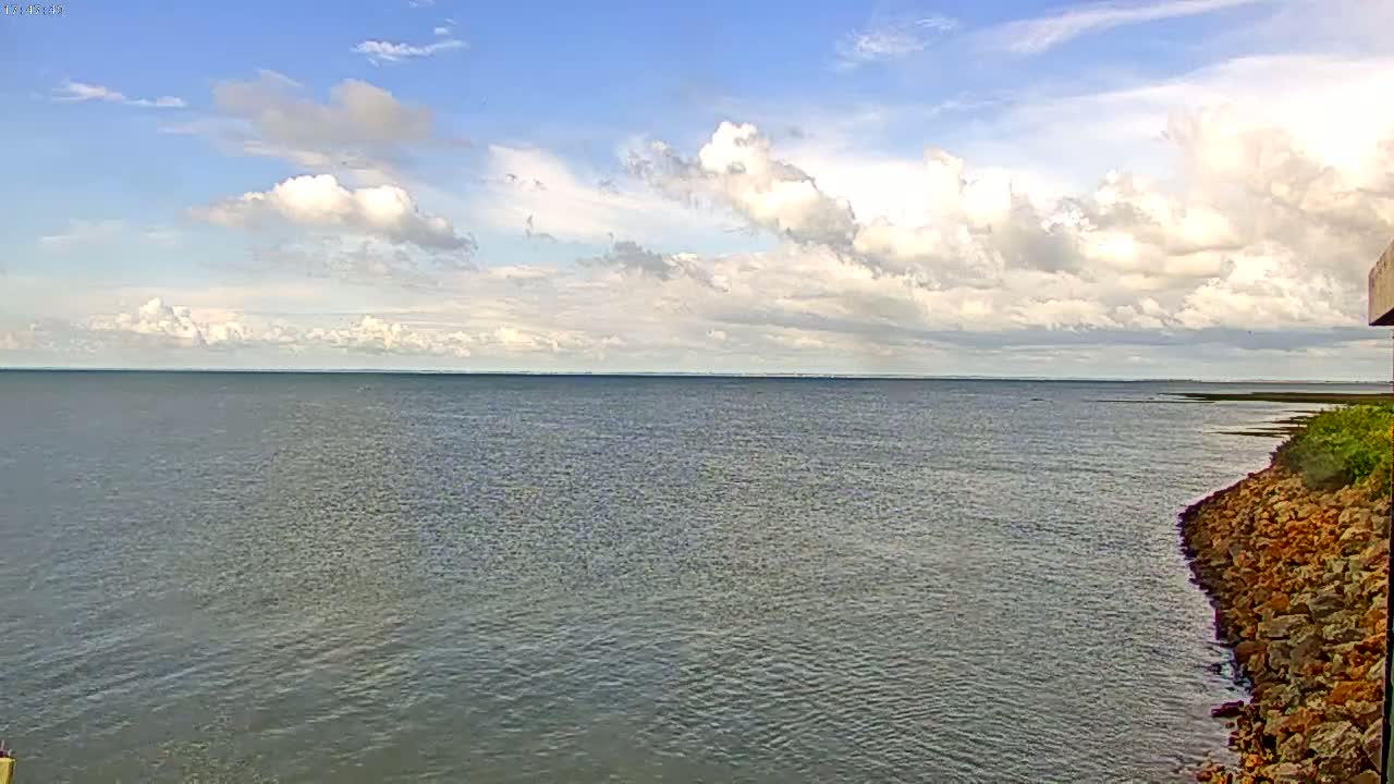 A calm body of water stretches to a distant horizon under a partly cloudy sky, with a rocky shoreline visible in the foreground.
