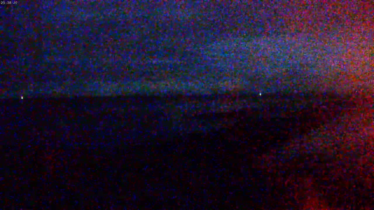 A dark, nighttime scene shows a horizon line separating a dark sky from a similarly dark land or water.