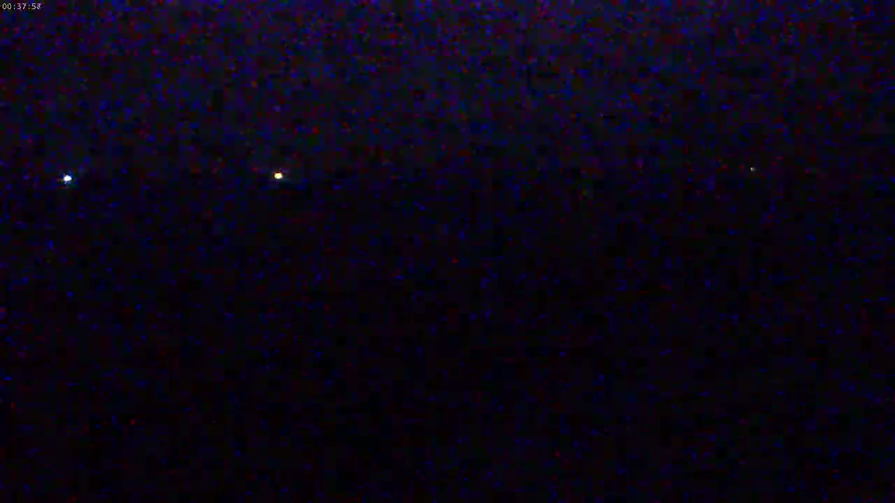 A dark, nighttime scene shows a few small, distant lights on the horizon.