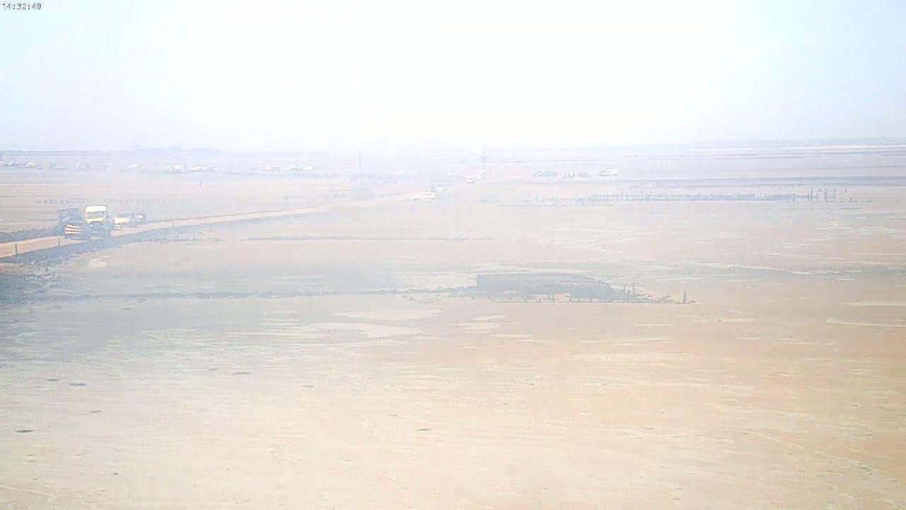 A hazy, flat landscape with a few vehicles on a distant road is visible under a bright, mostly clear sky.