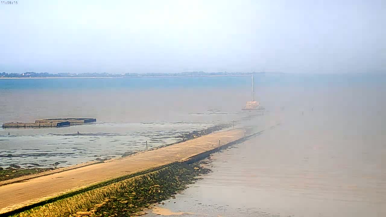 A long, sandy causeway extends into a hazy, misty body of water, with a distant shoreline visible in the background.