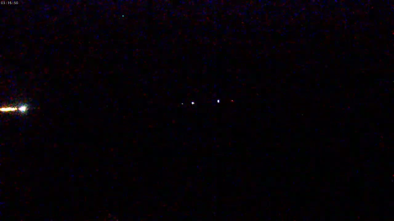 A nighttime image shows a bright light streaking across the left side and several fainter lights in the center.